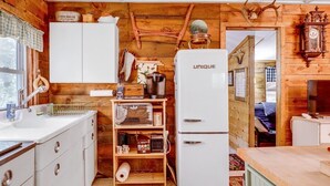 Una cocina rústica con paredes de madera, un refrigerador blanco, electrodomésticos antiguos y decoración de estilo campestre.