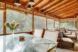 Un interior de madera con una mesa de vidrio, sillas de mimbre y un jarrón de flores.