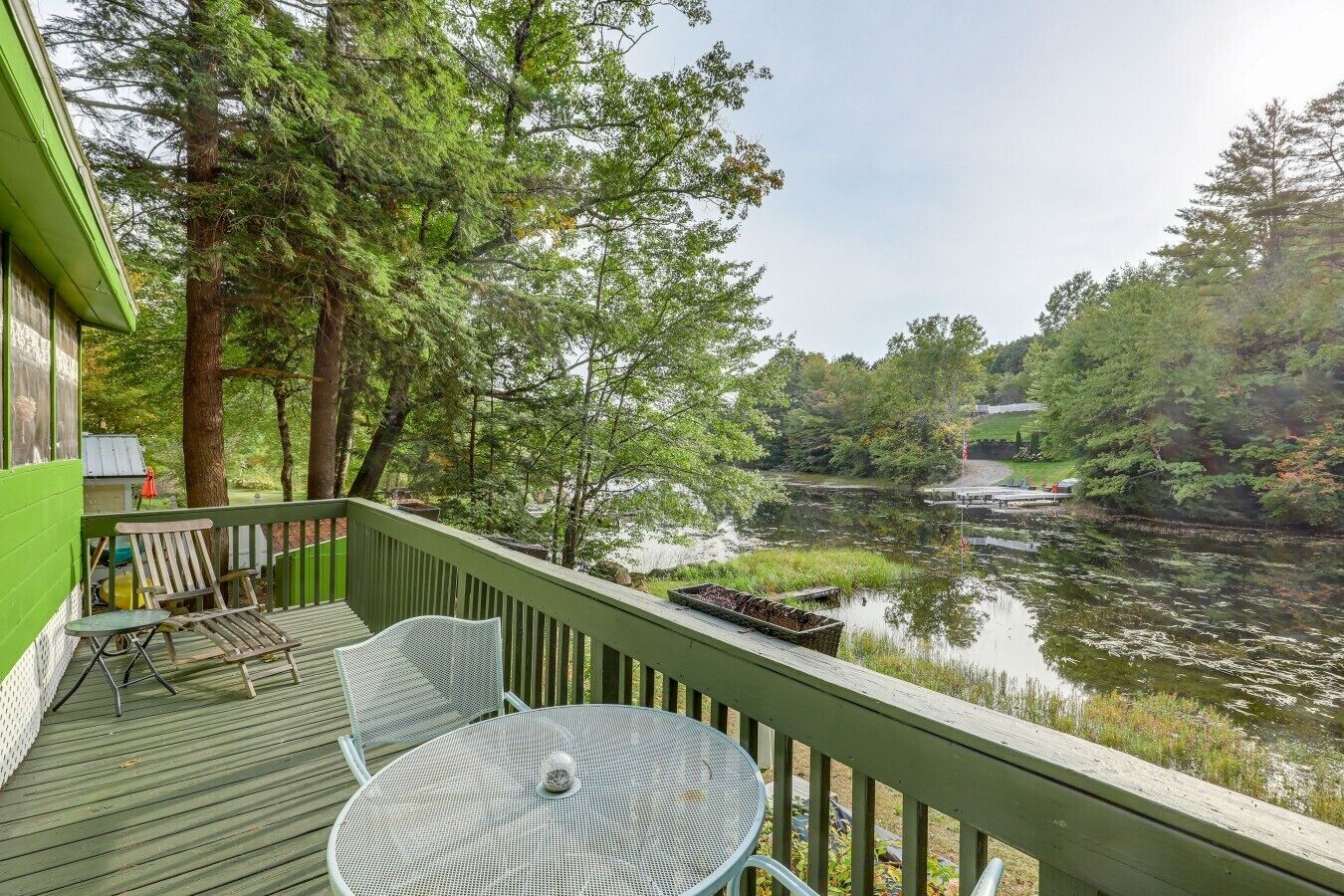 Une terrasse avec une table et des chaises donnant sur une étendue d’eau paisible, entourée d’arbres.