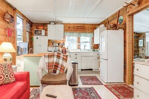 A cozy cabin interior with a kitchenette, a red sofa, and a plaid blanket on a chair.