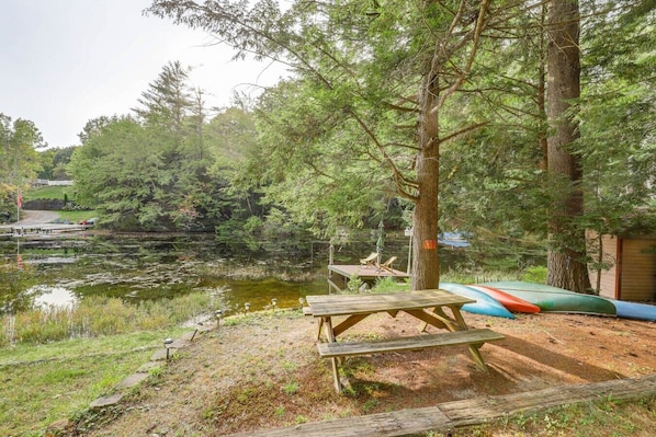 A picnic table and canoes by a lake with trees and a dock in the background.