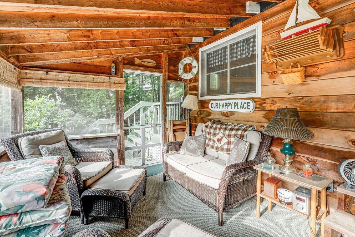 Interior acogedor de una cabaña con muebles de mimbre, techo de madera y vistas al exterior.