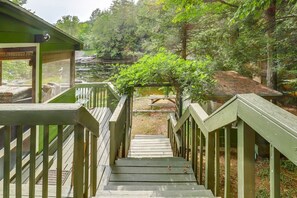 A wooden staircase leading to a building with a green roof, surrounded by trees and a pond.