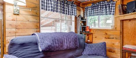 L’intérieur d’un chalet chaleureux, avec un canapé, des rideaux à carreaux, une lampe et une bibliothèque.