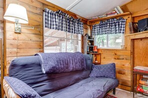 A cozy cabin interior with a sofa, checkered curtains, a lamp, and a bookshelf.
