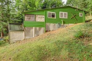 A green single-story house with a fenced yard, a wooden deck, and a hillside.
