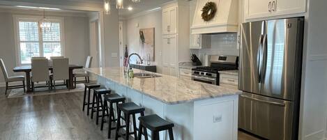 A modern kitchen with a central island, bar stools, stainless steel appliances, and pendant lighting.
