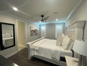 Quarto com cama, ventoinha no teto, espelho fixado na parede e janela com persianas.