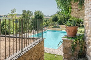 A swimming pool with a stone border, surrounded by a garden with a variety of plants and a view of the countryside. - New Apartment in Tuscany with a Pool and Breathtaking Views (Asciano)