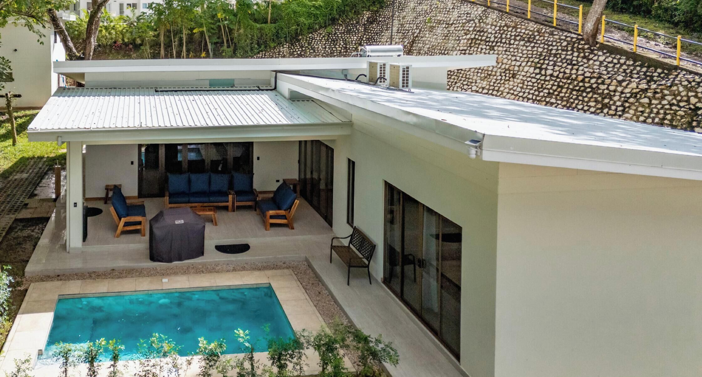 A modern house with a covered patio, a swimming pool, and a view of a rocky hillside.