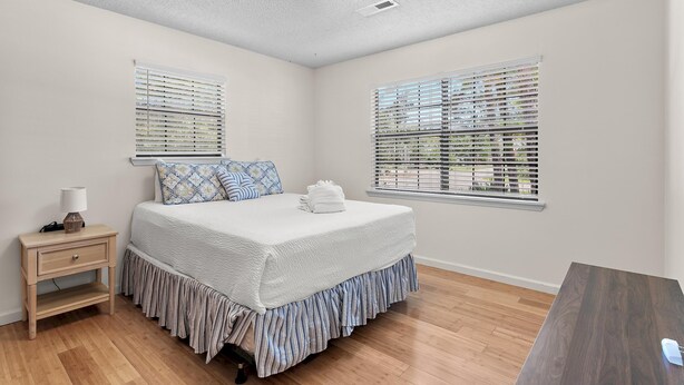 A bedroom with a bed, bedside table, lamp, and two windows with blinds. - Ash at the Beach (Santa Rosa Beach)