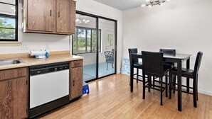A modern kitchen with wooden cabinets, a dishwasher, and a dining area with a table and chairs. - Ash at the Beach (Santa Rosa Beach)