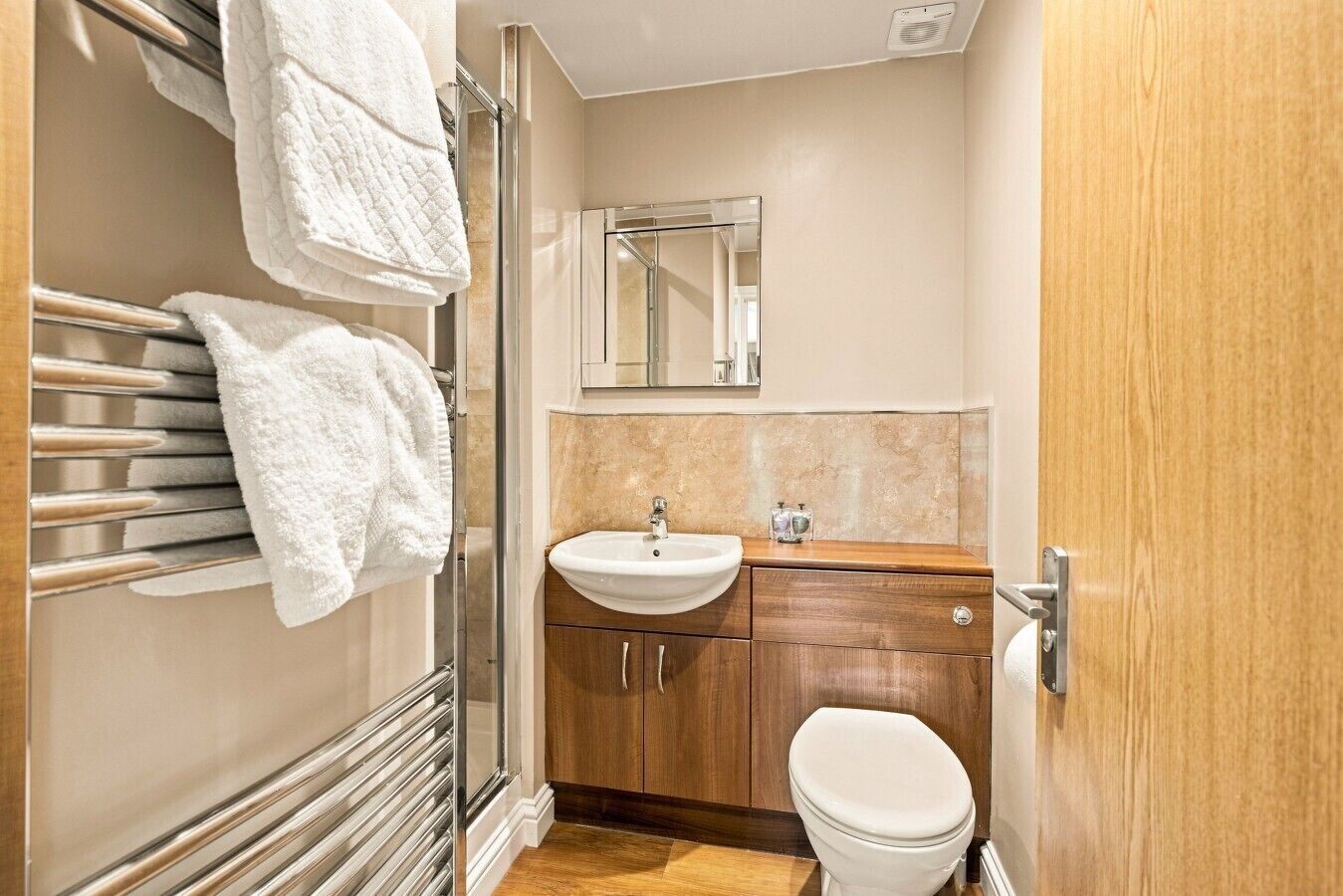 A bathroom with a glass shower enclosure, a white sink, a wooden vanity, and a toilet.