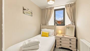A bedroom with a bed, bedside table, lamp, and a window with curtains.