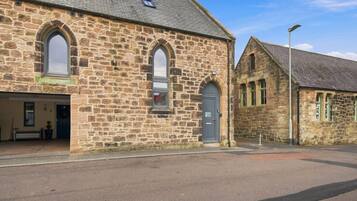 A stone building with arched windows and a door, a bench outside, and a clear sky.