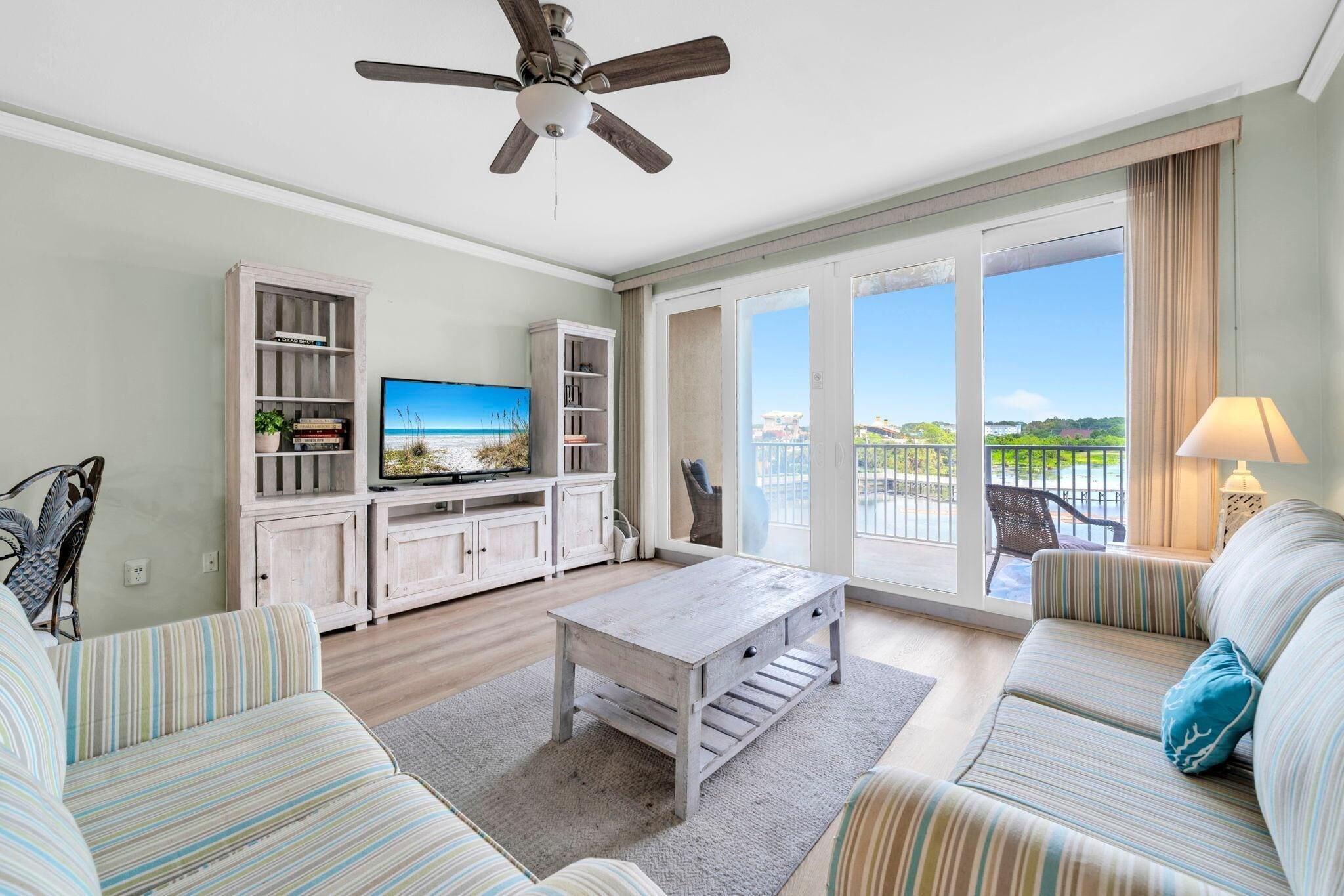 A spacious living room with a television, a ceiling fan, a sofa, a coffee table, and a balcony with a view.
