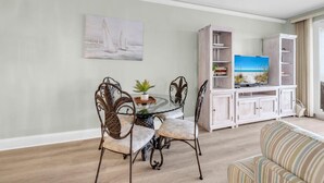Un coin repas avec une table ronde et des chaises, une bibliothèque avec un téléviseur et un tableau accroché au mur.