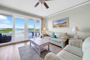 Ein geräumiges Wohnzimmer mit Blick auf ein Gewässer, einem Deckenventilator und einem Gemälde an der Wand.