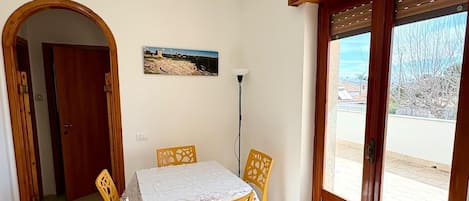 A dining area with a table and chairs, a picture on the wall, and a view through the door.