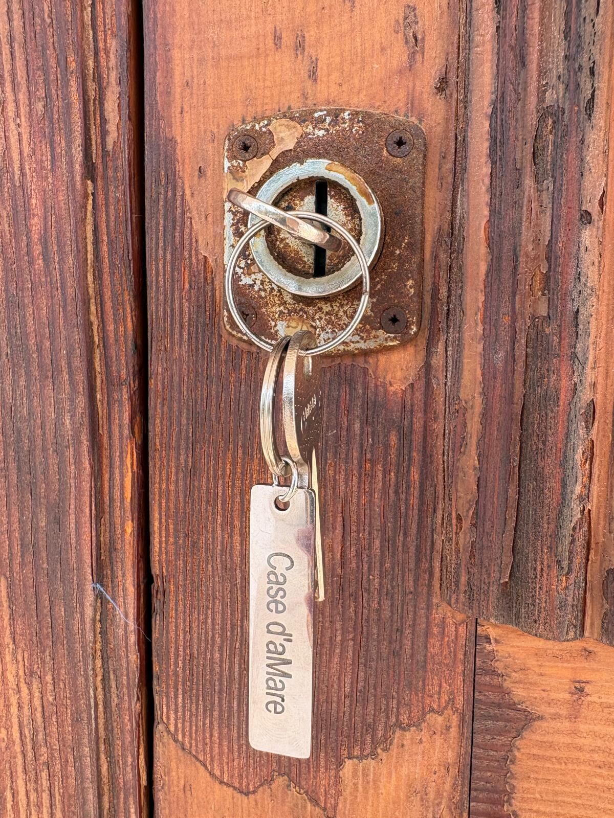Une poignée de porte en métal, avec un porte-clés et une plaque métallique portant l’inscription « Case d’Amare ».
