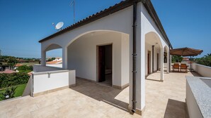Et overdækket udendørs område med terrasse, en dør der fører ind, og en parabolantenne på taget.