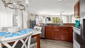 A kitchen with wooden cabinets, a white countertop, a dishwasher, and a dining area with a table and chairs. - Crystal Village II 15B (Miramar Beach)