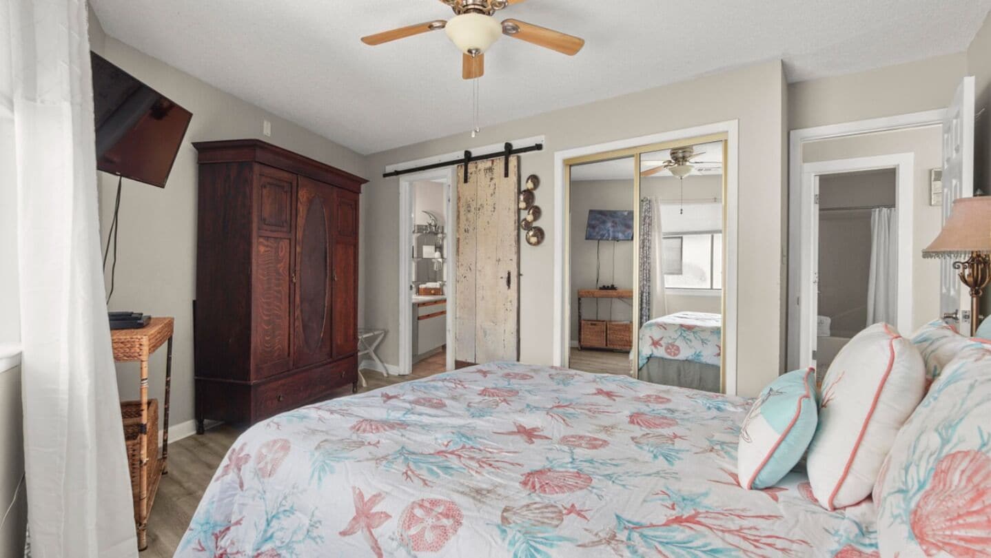 A bedroom with a bed, a ceiling fan, a wardrobe, and a sliding door leading to a bathroom.