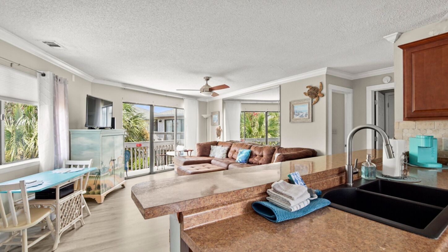 A modern kitchen with a large island, a dining area with a table and chairs, and a living area with a sofa and a ceiling fan.