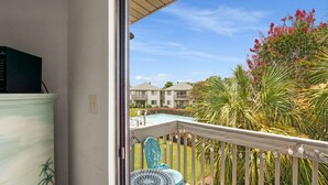 A balcony with a view of a swimming pool, palm trees, and a building in the background. - Crystal Village II 15B (Miramar Beach)