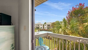 Ein Balkon mit Blick auf einen Swimmingpool, Palmen und ein Gebäude im Hintergrund.