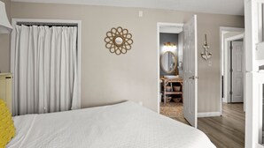 A bedroom with a bed, a bathroom with a mirror, and a door leading to another room. - Crystal Village II 15B (Miramar Beach)