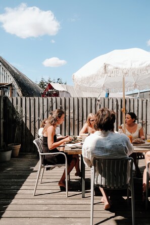 A group of people dining at an outdoor table with a wooden deck and a white umbrella. - bumpkin. Stylish Coastal Home. Walk to Beach & Award-Winning Seafood. Sleeps 6 (West Mersea)