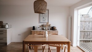 Zona pranzo con tavolo in legno, sedie, lampadario a sospensione e un poster dell'alfabeto appeso al muro.