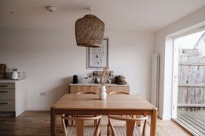 A dining area with a wooden table, chairs, a hanging light fixture, and a wall-mounted alphabet poster. - bumpkin. Stylish Coastal Home. Walk to Beach & Award-Winning Seafood. Sleeps 6 (West Mersea)