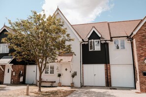 A residential building with a brick facade, white garage doors, and a tree in the front yard. - bumpkin. Stylish Coastal Home. Walk to Beach & Award-Winning Seafood. Sleeps 6 (West Mersea)