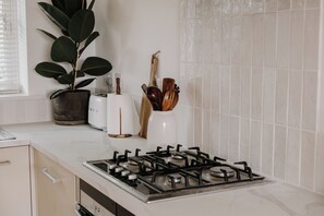 A kitchen with a gas stove, a potted plant, a toaster, and wooden utensils on the counter. - bumpkin. Stylish Coastal Home. Walk to Beach & Award-Winning Seafood. Sleeps 6 (West Mersea)