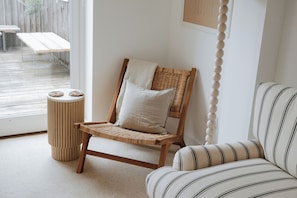 A room with a wicker chair, a striped sofa, a small round table, and a wall-mounted picture. - bumpkin. Stylish Coastal Home. Walk to Beach & Award-Winning Seafood. Sleeps 6 (West Mersea)