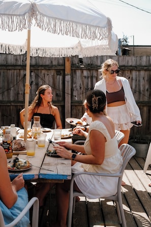 Un espace extérieur aménagé pour les repas, avec une table en bois, des chaises et un parasol blanc.
