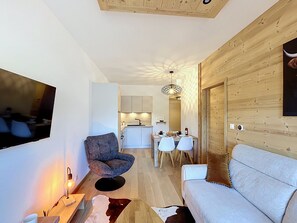Een moderne woonkamer met een bank, een stoel, een televisie en een eethoek met een tafel en stoelen.