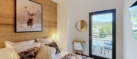 A bedroom with a bed, a framed deer picture, a round mirror, and a view of a balcony.