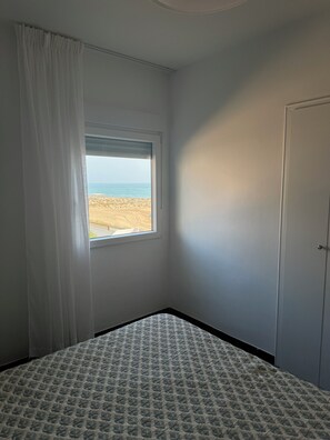 A bedroom with a single bed, a window with a view of the beach, and a door.