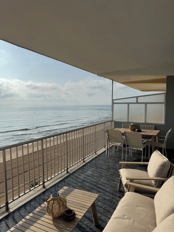 A balcony with a view of the sea, furnished with a table, chairs, and a sofa.