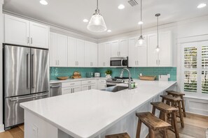 Una cocina moderna con armarios blancos, electrodomésticos de acero inoxidable, una isla grande con taburetes de bar e iluminación colgante.