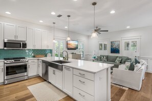 A modern kitchen with white cabinetry, a built-in oven, a microwave, and a large island with a sink. - Discover Southern Tides with Bonheur Vacations! (Watersound)