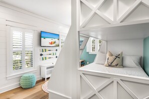 Un dormitorio con literas, un televisor en la pared, un escritorio y una ventana con contraventanas.