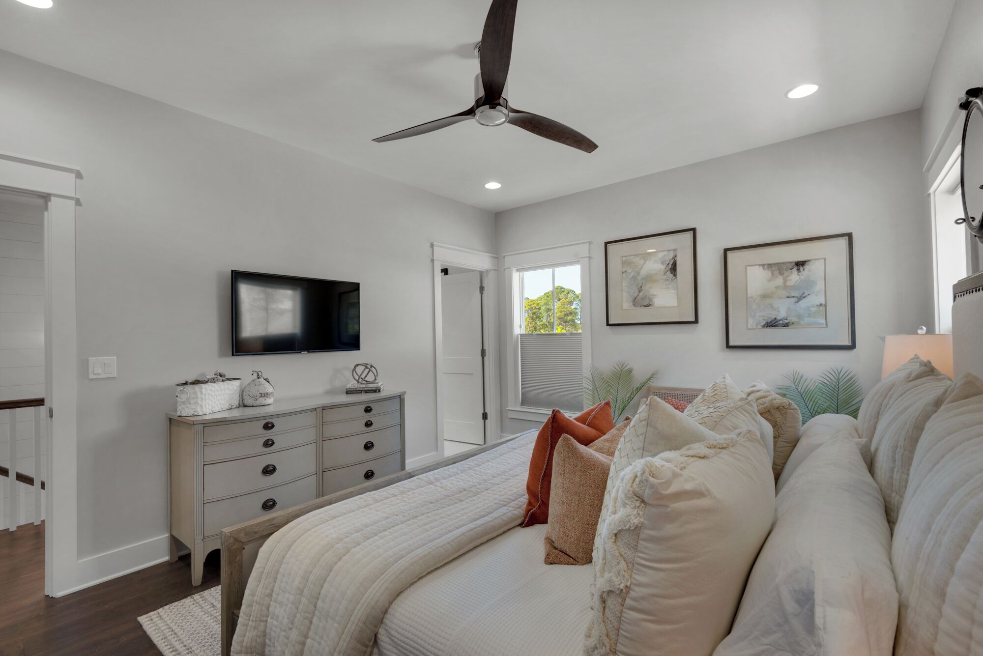 Ein Schlafzimmer mit Bett, Kommode, Deckenventilator, Fernseher und Kunstwerken.
