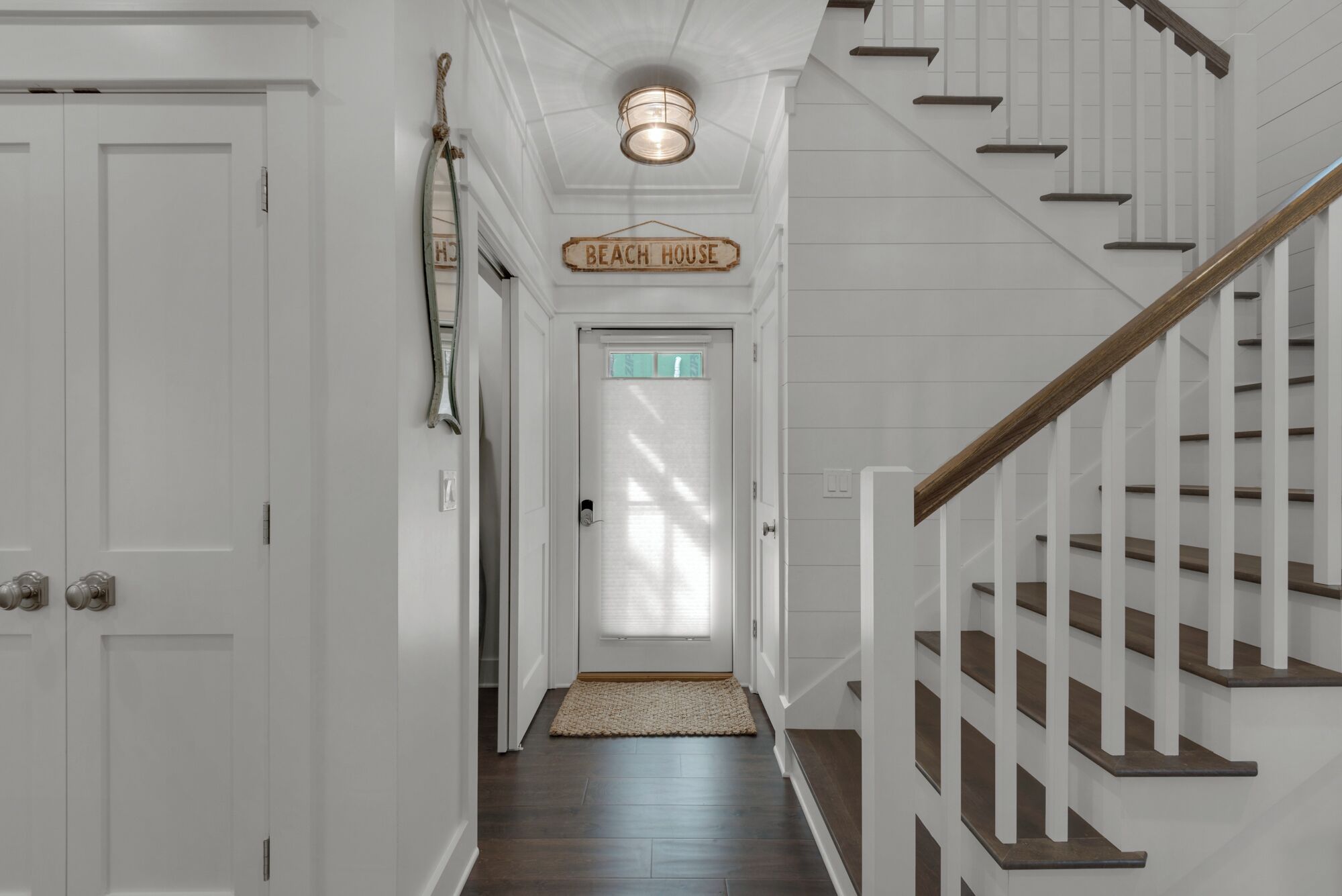 Un couloir avec un escalier en bois, une pancarte indiquant « Chaque maison », et une porte avec du verre dépoli.