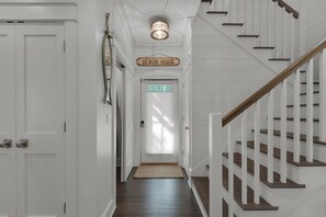 En hall med en trätrappa, en skylt med texten ”Varje hus” och en dörr med frostat glas.