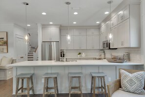 A modern kitchen with white cabinetry, a stainless steel refrigerator, and a large island with bar stools. - Set Sail for Goin’ Coastal pet friendly 3 bedroom luxury home (Watersound)