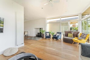 A spacious living room with a large window, a ceiling fan, and a variety of seating options including armchairs and a sofa. - Lakeside Villa w/ Pool & Tennis in Cotswolds (Gloucestershire)